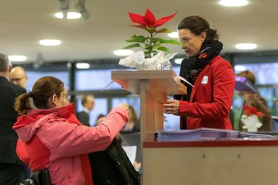 Zwei Frauen sind am Emfpangstresen, auf dem Tisch stehen rote Blumen